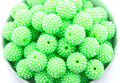 A close-up of many bright lime green beaded round craft beads piled together in a white bowl against a white background.