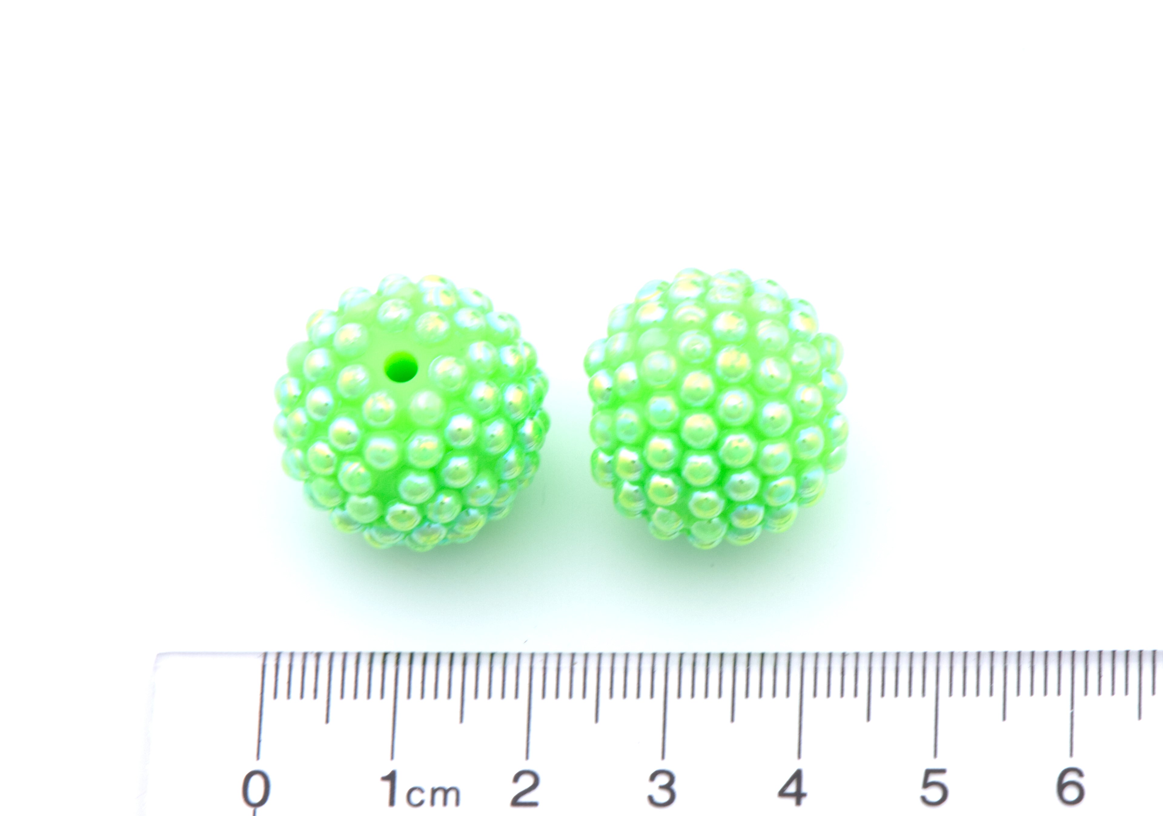 Two bright green beaded round beads shown on a white background with a cm ruler at the bottom for scale.