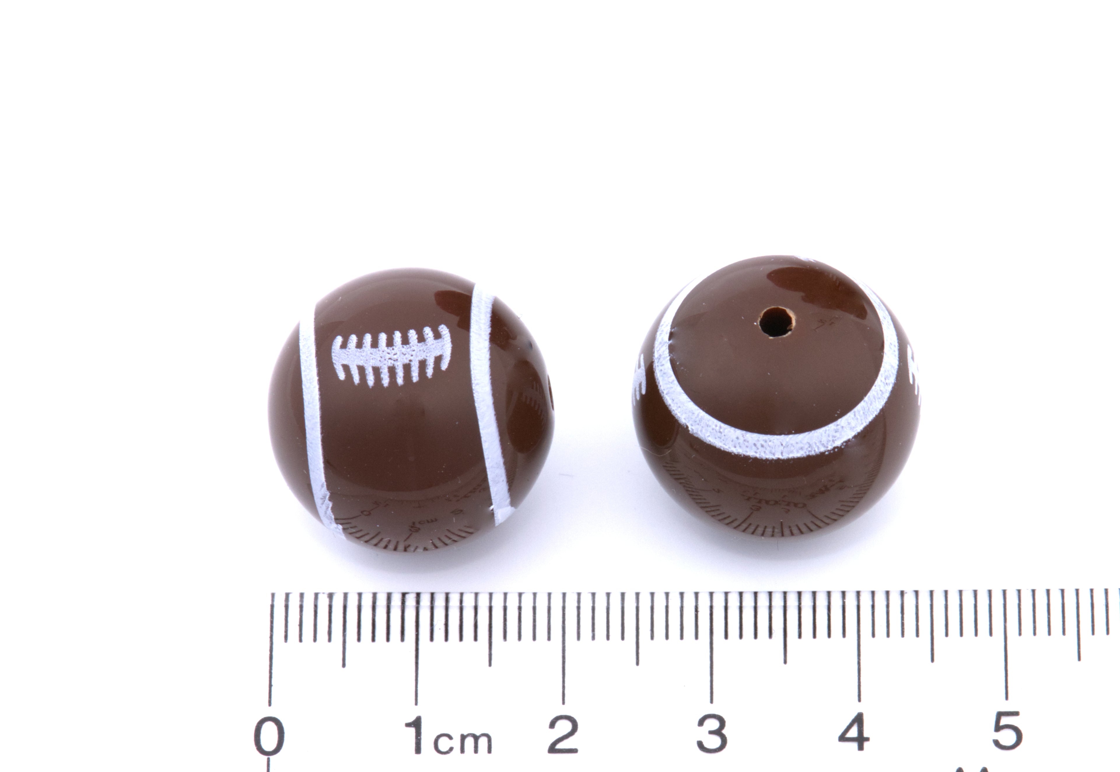Two brown football beads next to a ruler for scale on a white background 