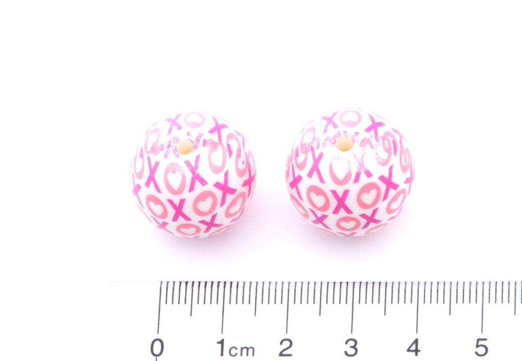 Pink beads with 'XOXO' pattern next to a ruler for scale on a white background