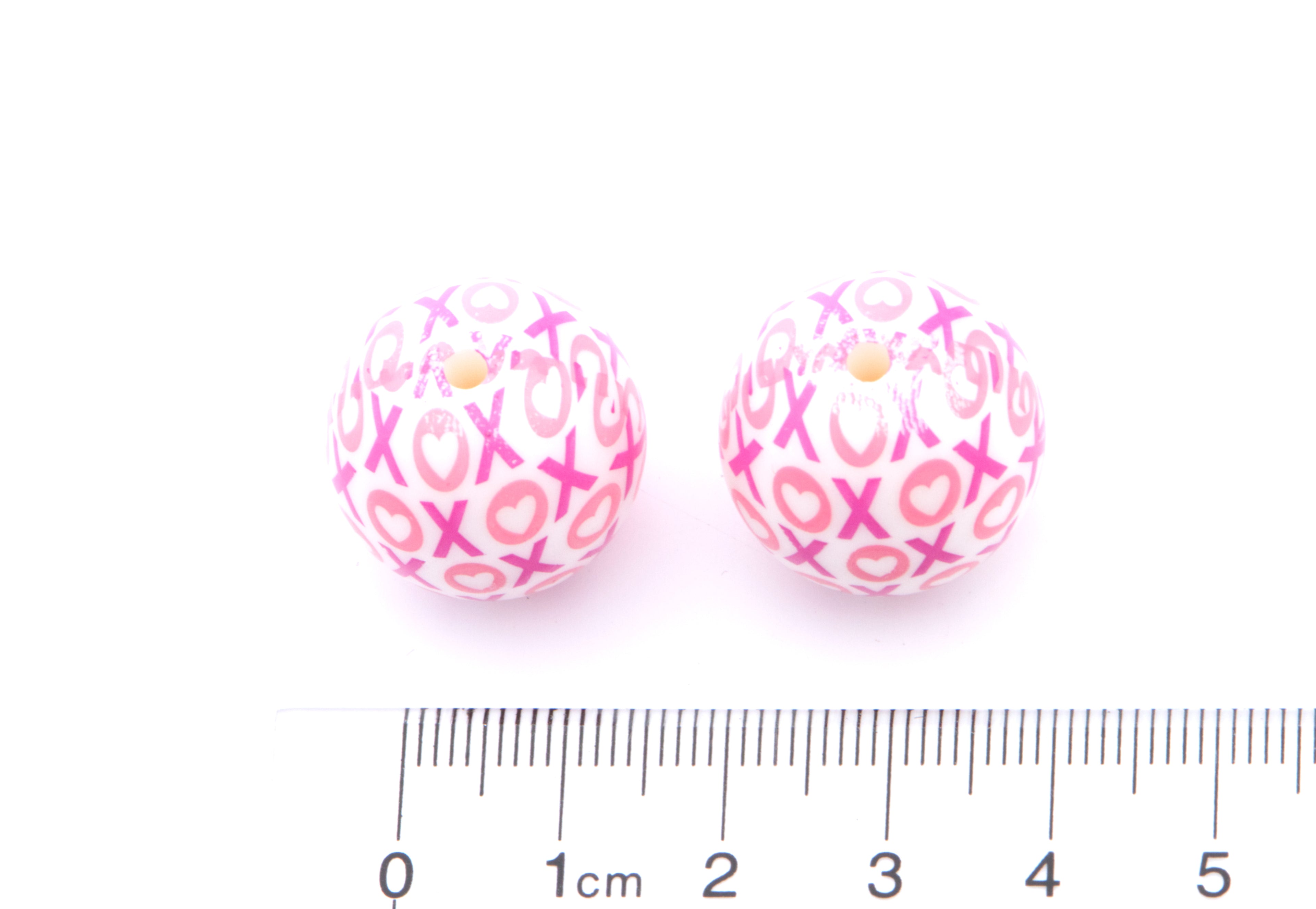 Pink beads with 'XOXO' pattern next to a ruler for scale on a white background