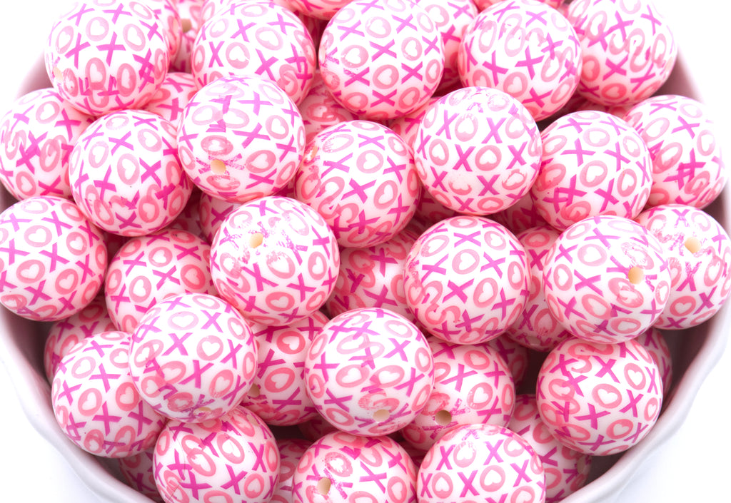 Pink beads with XOXO print in a white bowl on a white background