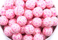 Pink beads with XOXO print in a white bowl on a white background