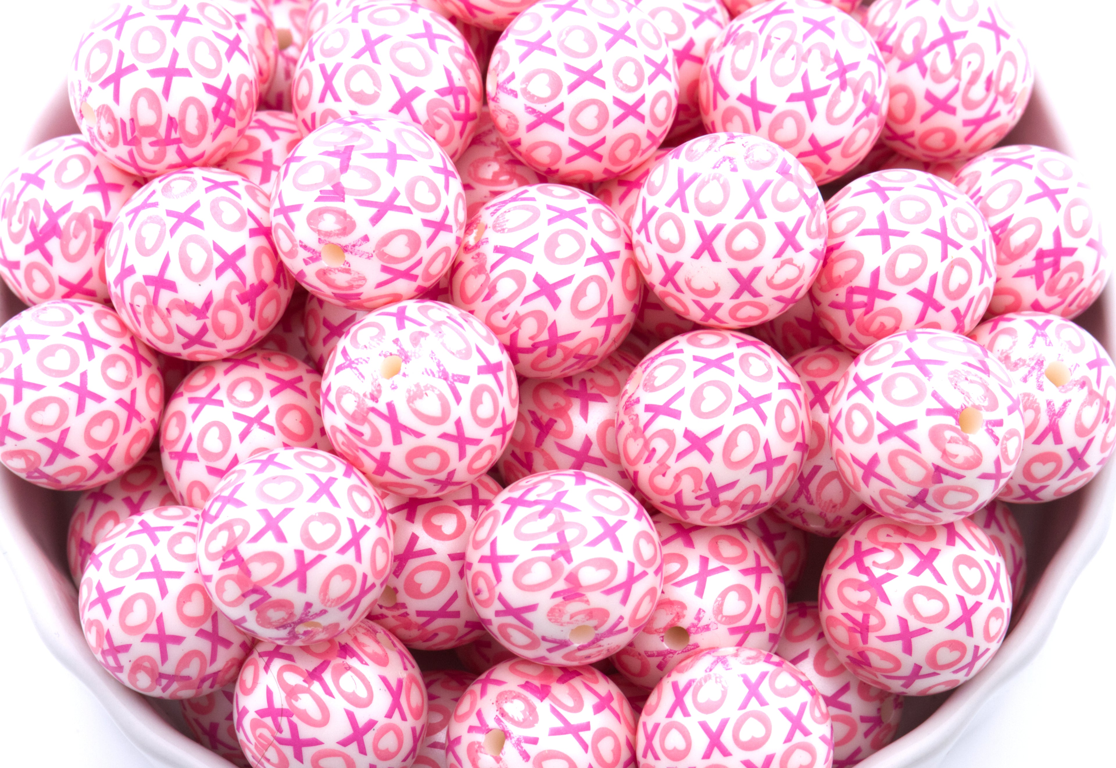 Pink beads with XOXO print in a white bowl on a white background