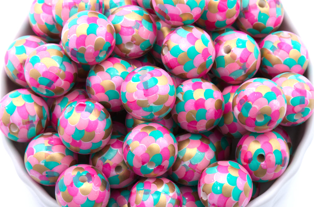 A close-up of many round mermaid scale print bubblegum beads with pink, teal, and gold scales, filling the frame.
