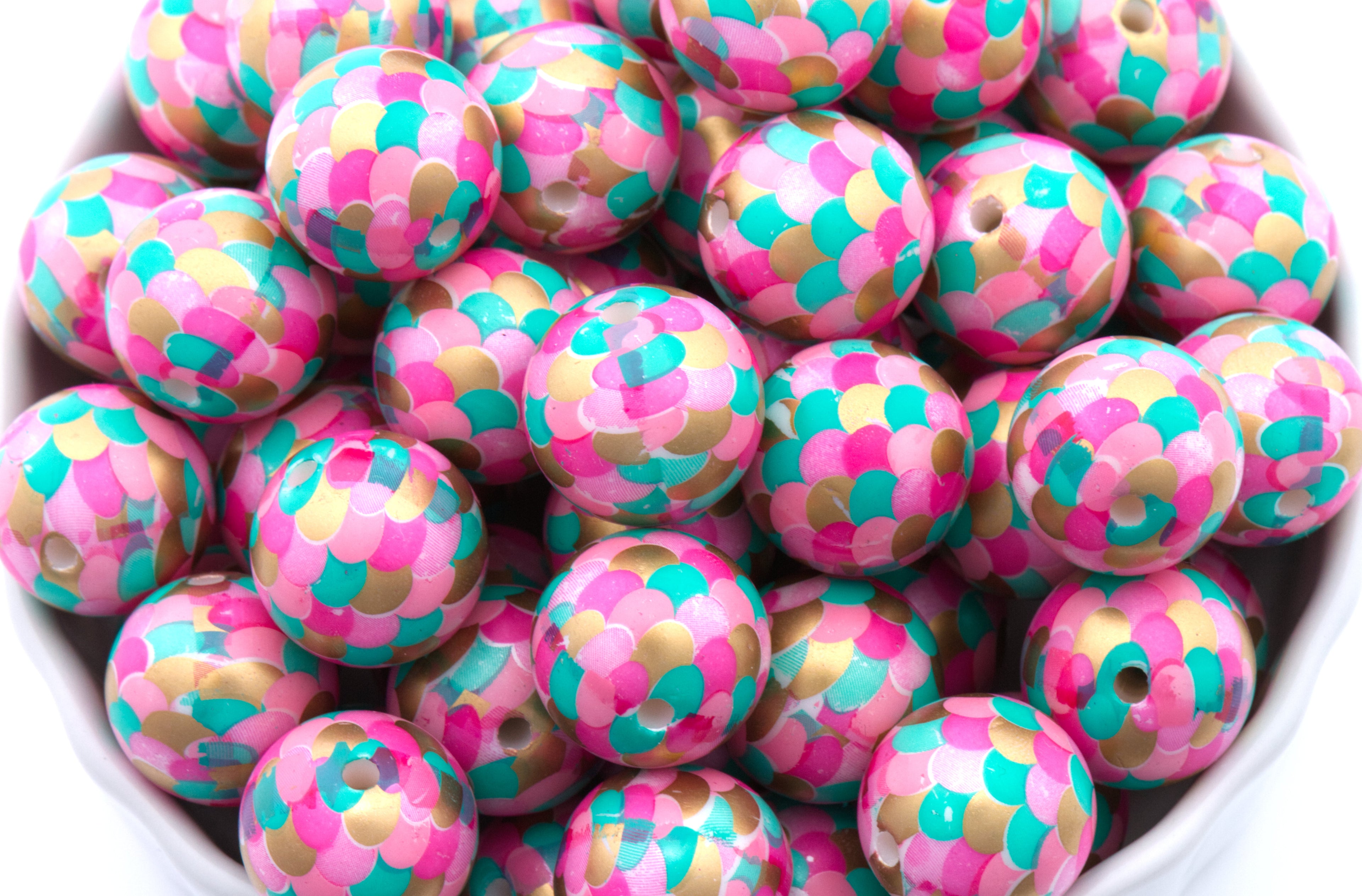 A close-up of many round mermaid scale print bubblegum beads with pink, teal, and gold scales, filling the frame.