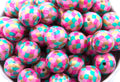 A close-up of many round mermaid scale print bubblegum beads with pink, teal, and gold scales, filling the frame.