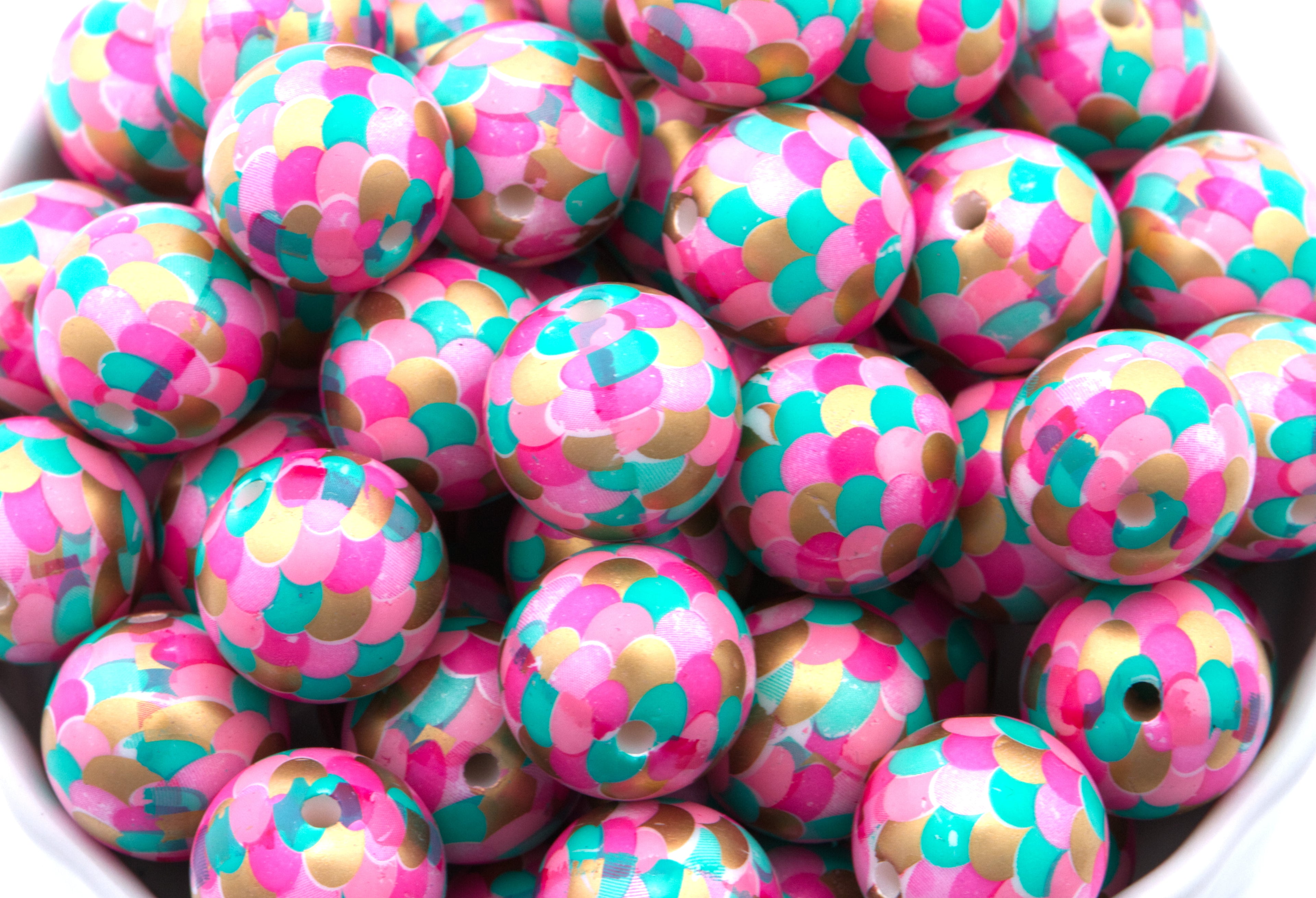 A close-up of many round mermaid scale print bubblegum beads with pink, teal, and gold scales, filling the frame.