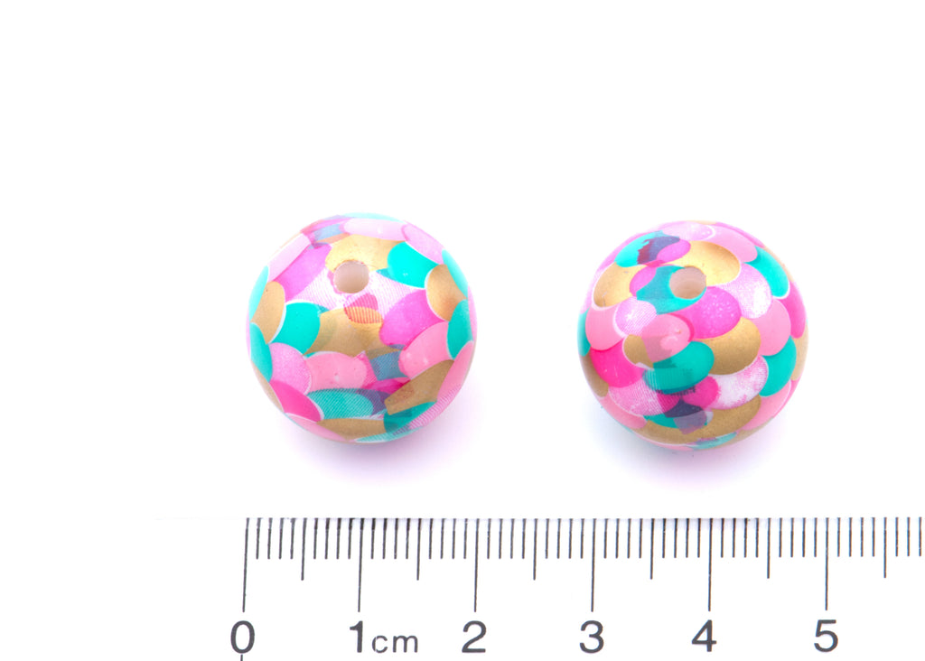 Two round mermaid scale bubblegum beads in a pattern of pink, teal, and gold, shown next to cm ruler for scale on a white background.