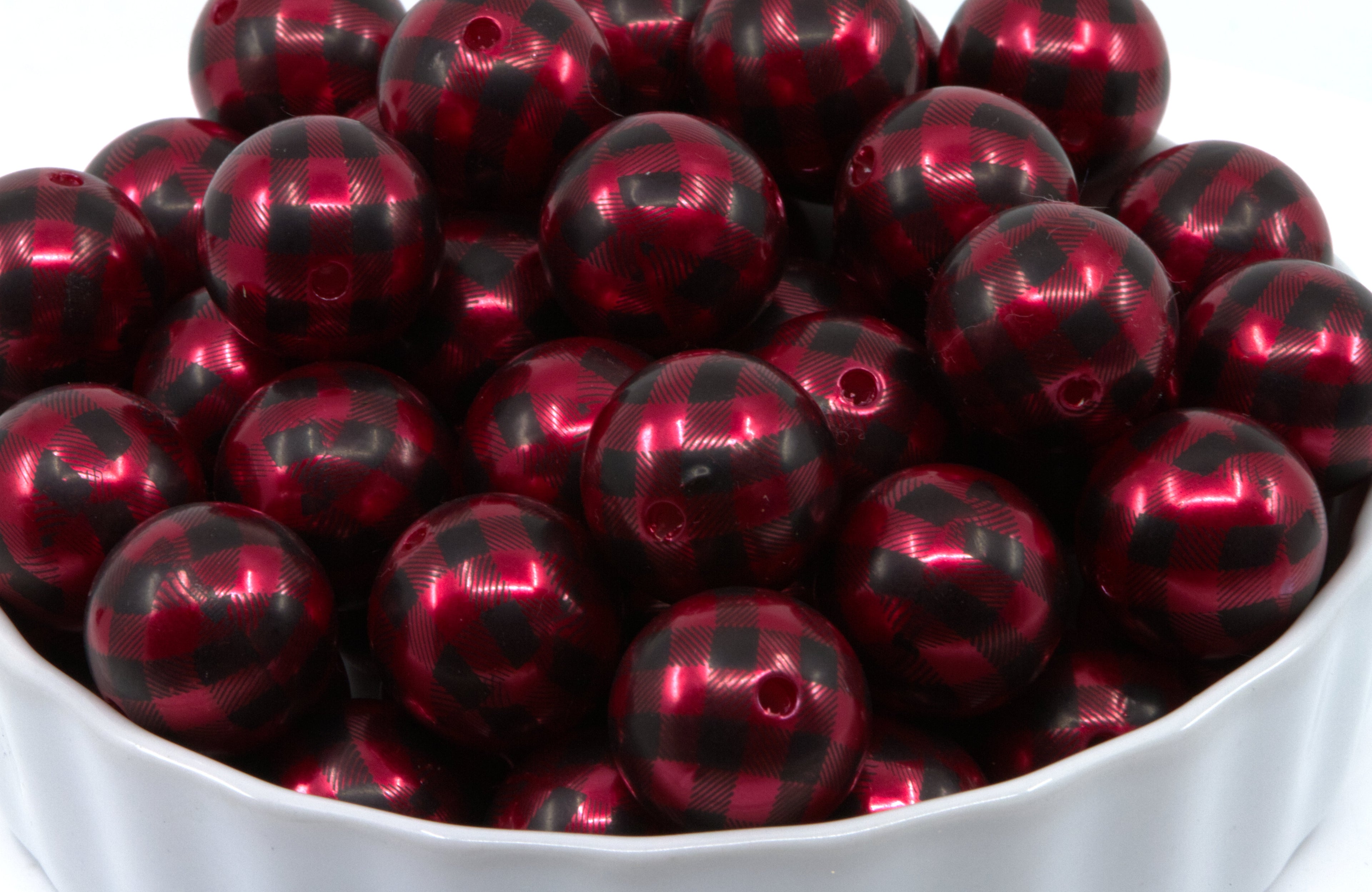 A white bowl filled with red and black buffalo plaid round beads on a white background.