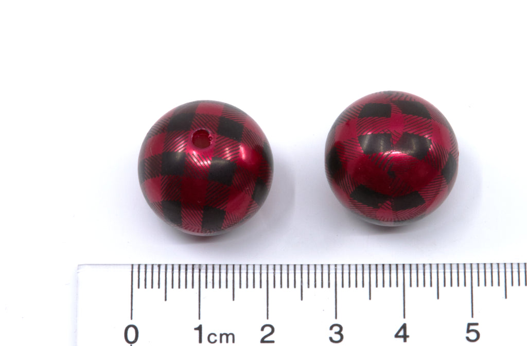 Two round red and black buffalo plaid beads with a central hole, shown next to a cm ruler for scale on a white background.