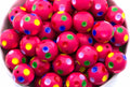 A close-up of many pink beads with colorful printed polka dots in yellow, green, blue, and white, piled together in a white container.