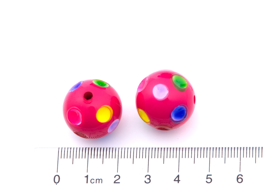 Two round pink beads with colorful printed polka dots, shown next to a cm ruler for scale on a white background.