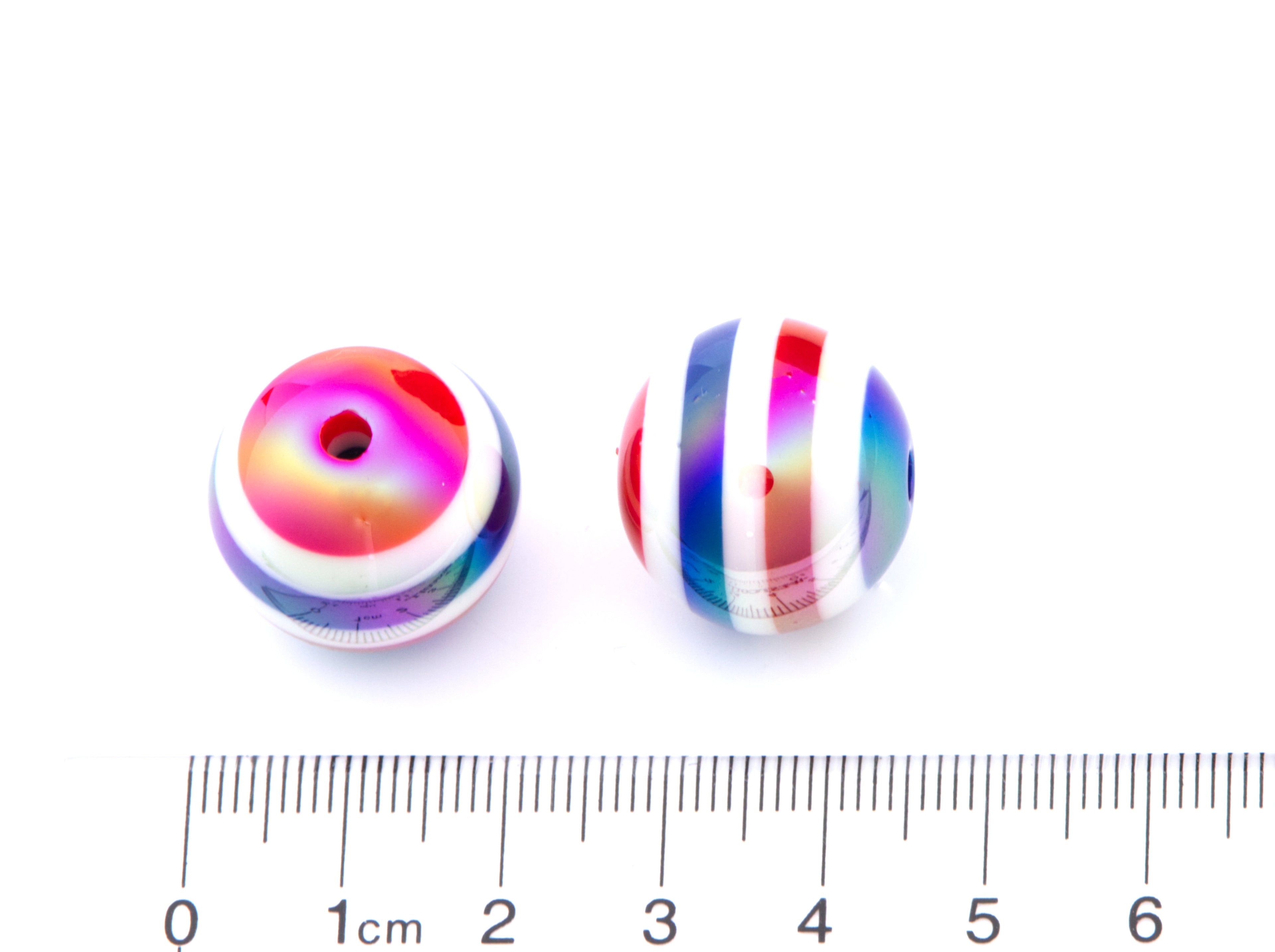 Two colorful striped beads in red, white and blue with a ruler for scale on a white background