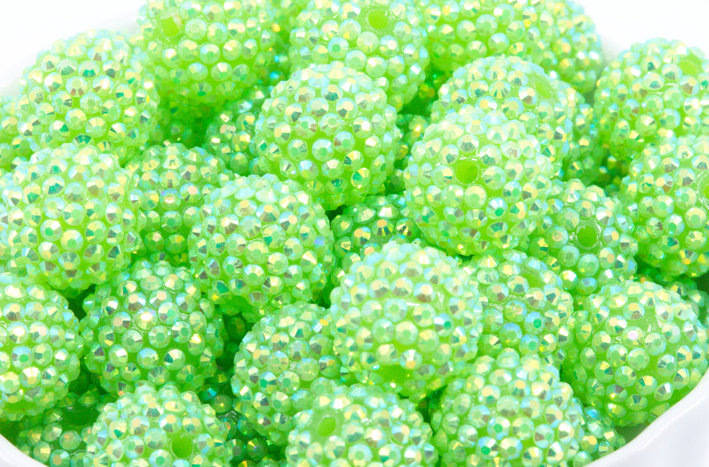 A close-up of many small round beads covered in iridescent rhinestones, filling the frame. The beads are bright lime green shown on a white background. 
