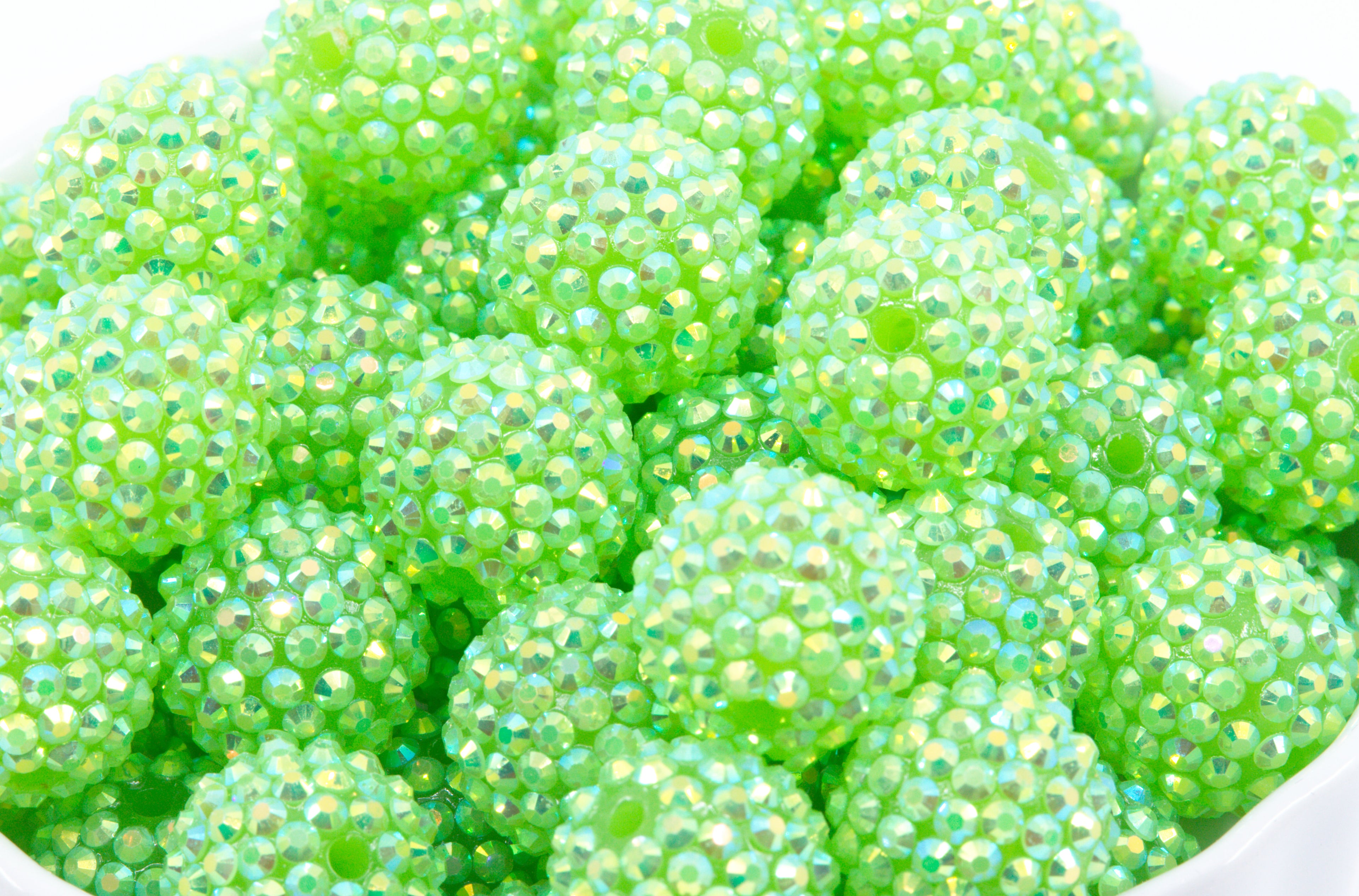 A close-up of many small round beads covered in iridescent rhinestones, filling the frame. The beads are bright lime green shown on a white background. 