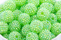 A close-up of many small round beads covered in iridescent rhinestones, filling the frame. The beads are bright lime green shown on a white background. 