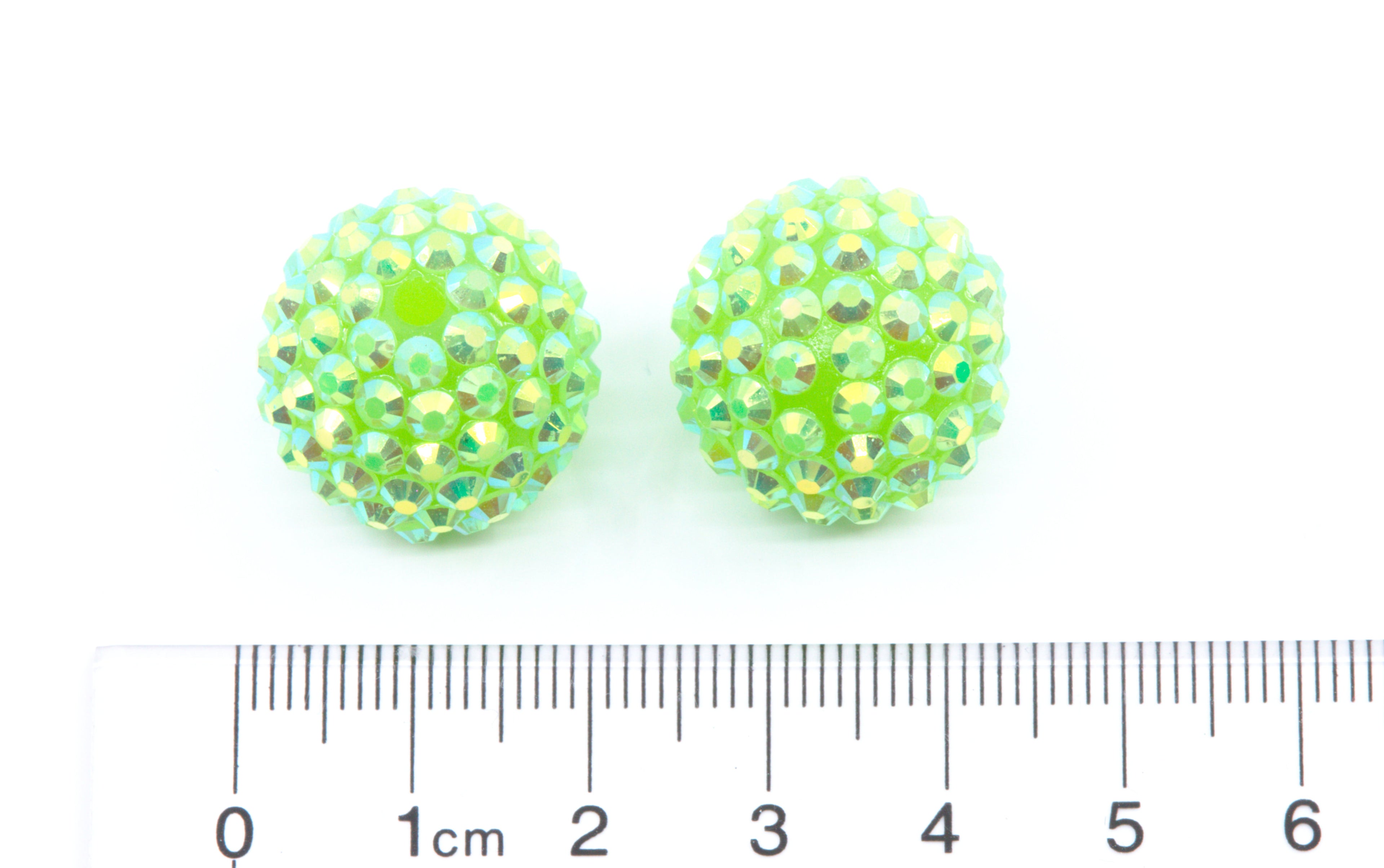 Two round lime rhinestone beads, shown above a cm ruler for scale on a white background.