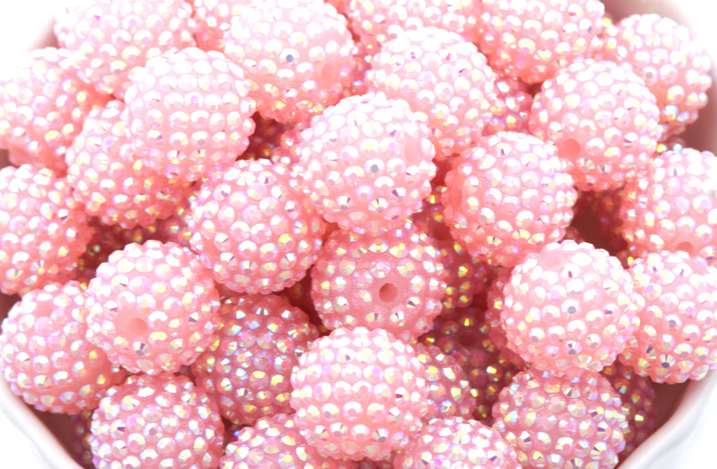 A close-up of multiple round pink beads covered in tiny iridescent rhinestones, filling the frame.