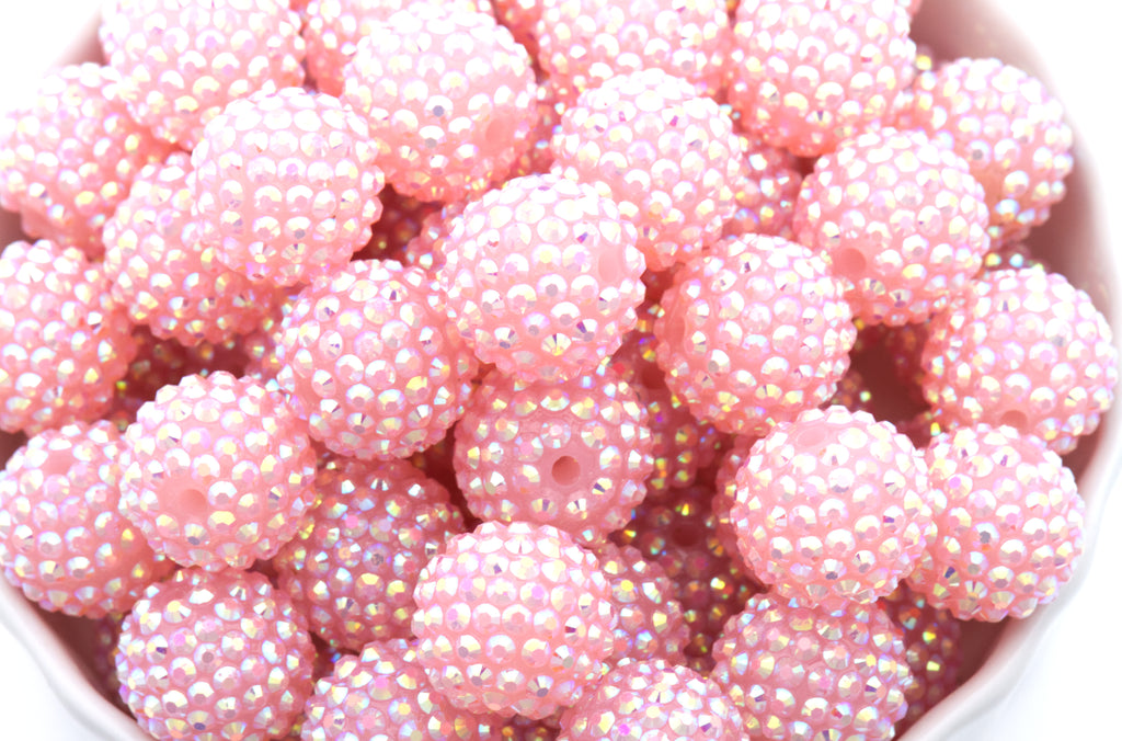 A close-up of multiple round pink beads covered in tiny iridescent rhinestones, filling the frame.