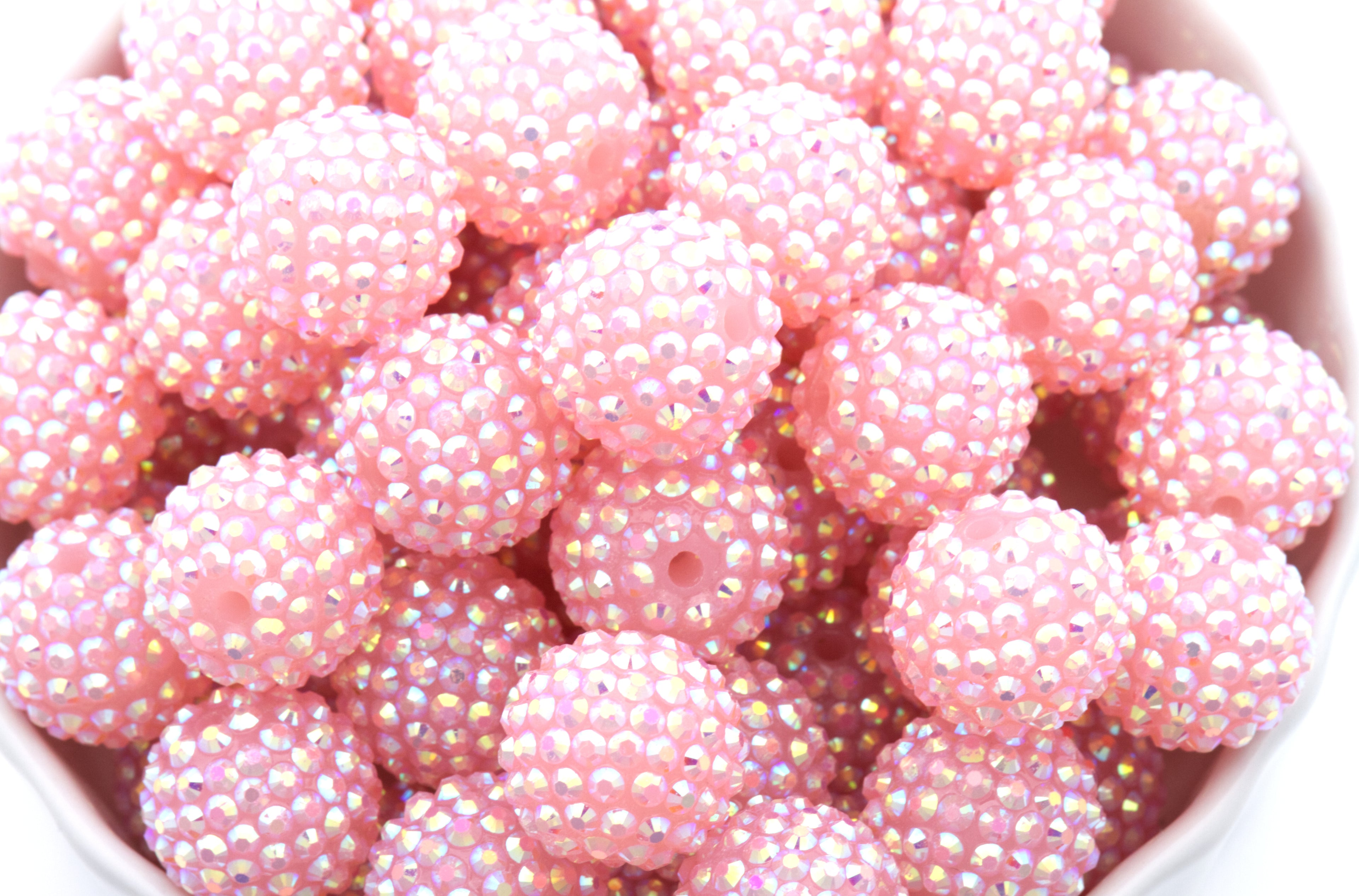 A close-up of multiple round pink beads covered in tiny iridescent rhinestones, filling the frame.