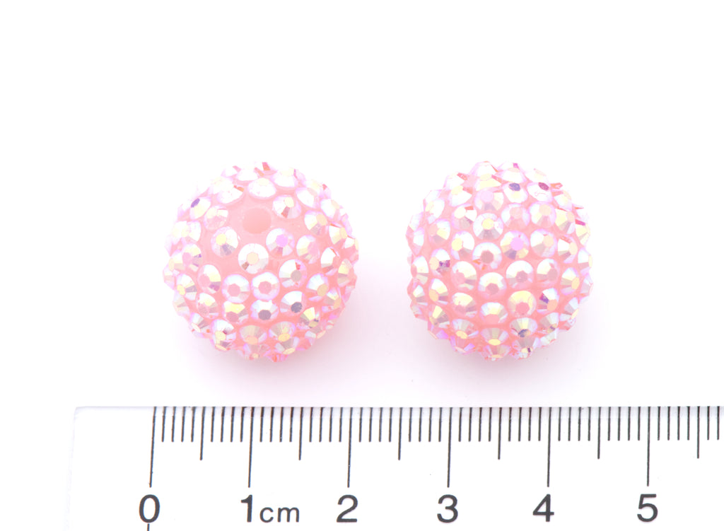 Two round pink rhinestone-covered beads shown next to a cm ruler for scale on a white background.