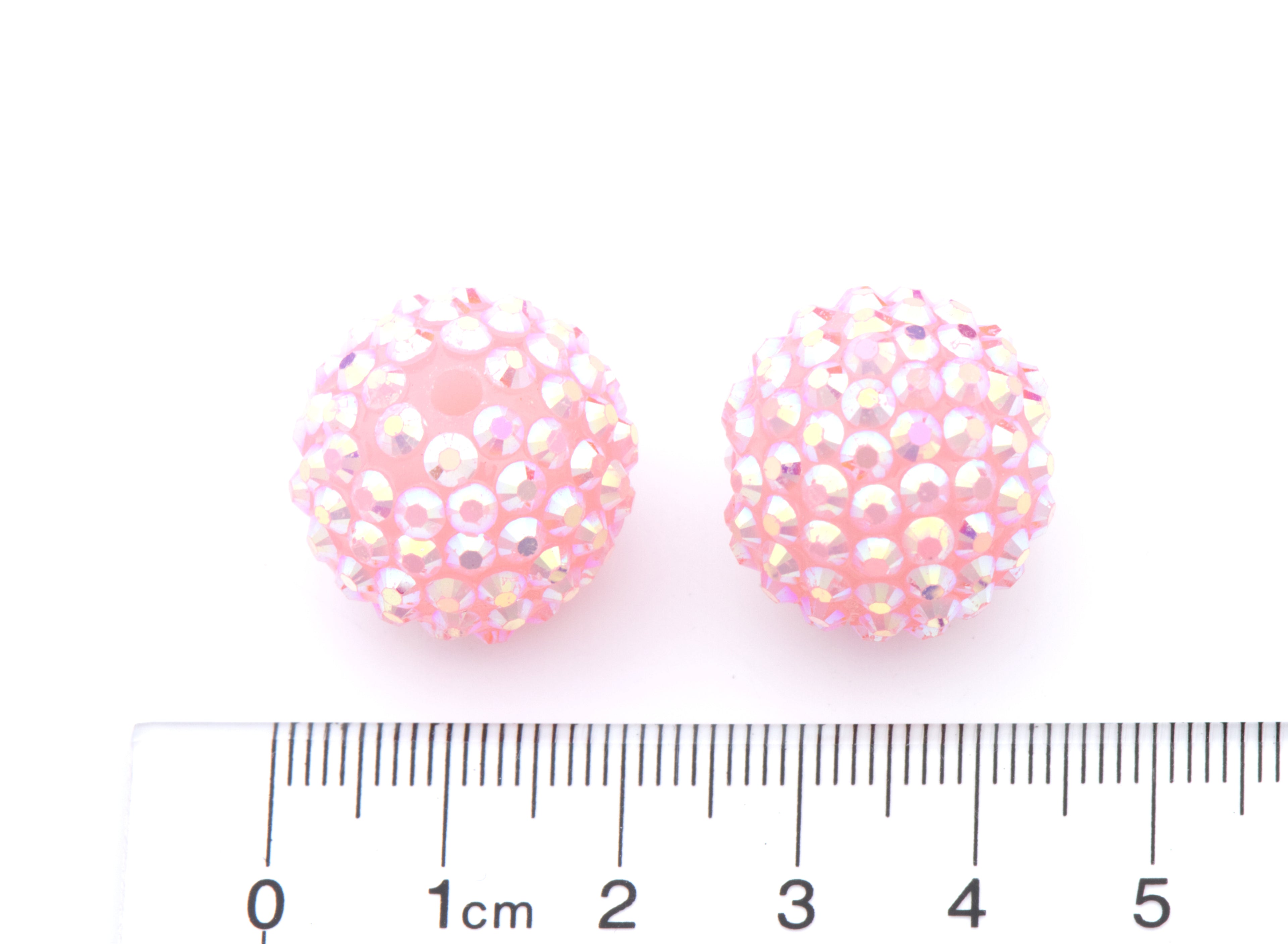 Two round pink rhinestone-covered beads shown next to a cm ruler for scale on a white background.