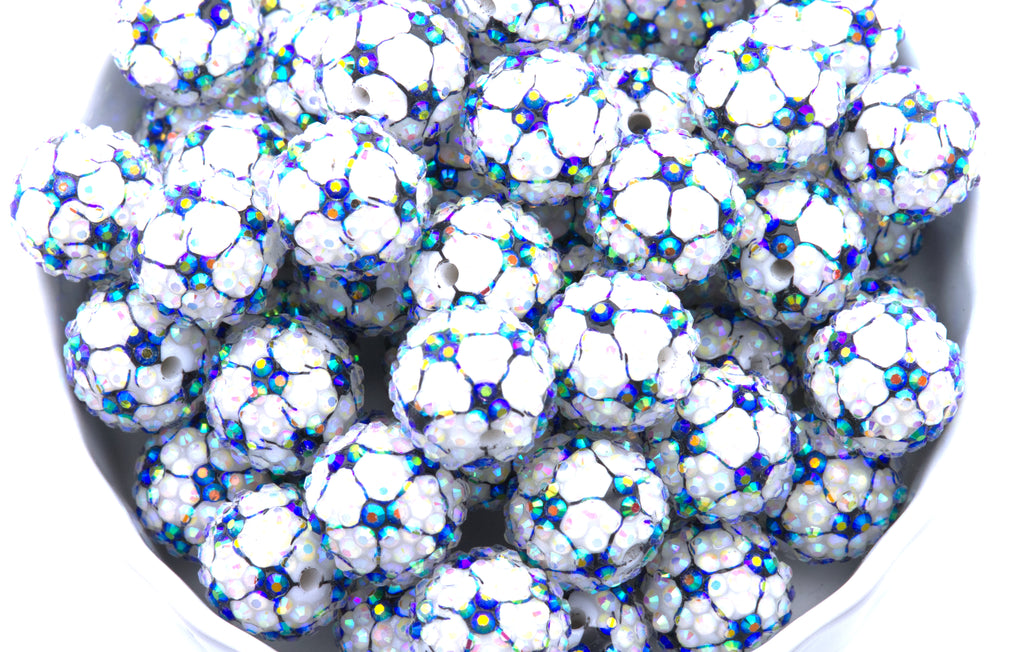 A close-up of soccer ball rhinestone beads, piled inside a white bowl on a white background.