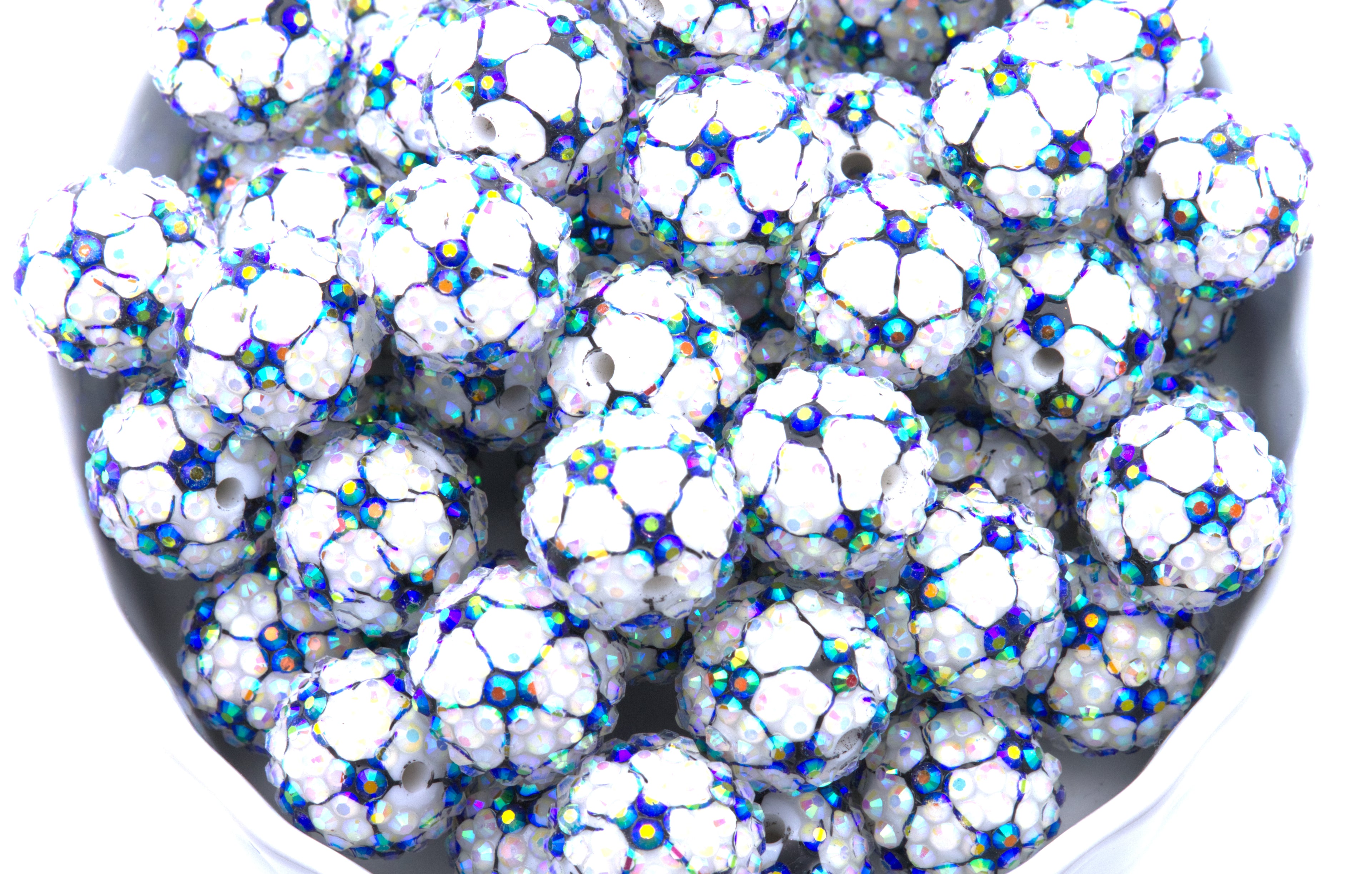 A close-up of soccer ball rhinestone beads, piled inside a white bowl on a white background.