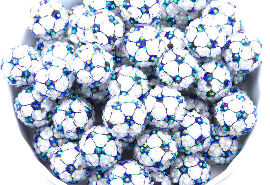 A close-up of soccer ball rhinestone beads, piled inside a white bowl on a white background.
