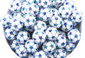 A close-up of soccer ball rhinestone beads, piled inside a white bowl on a white background.