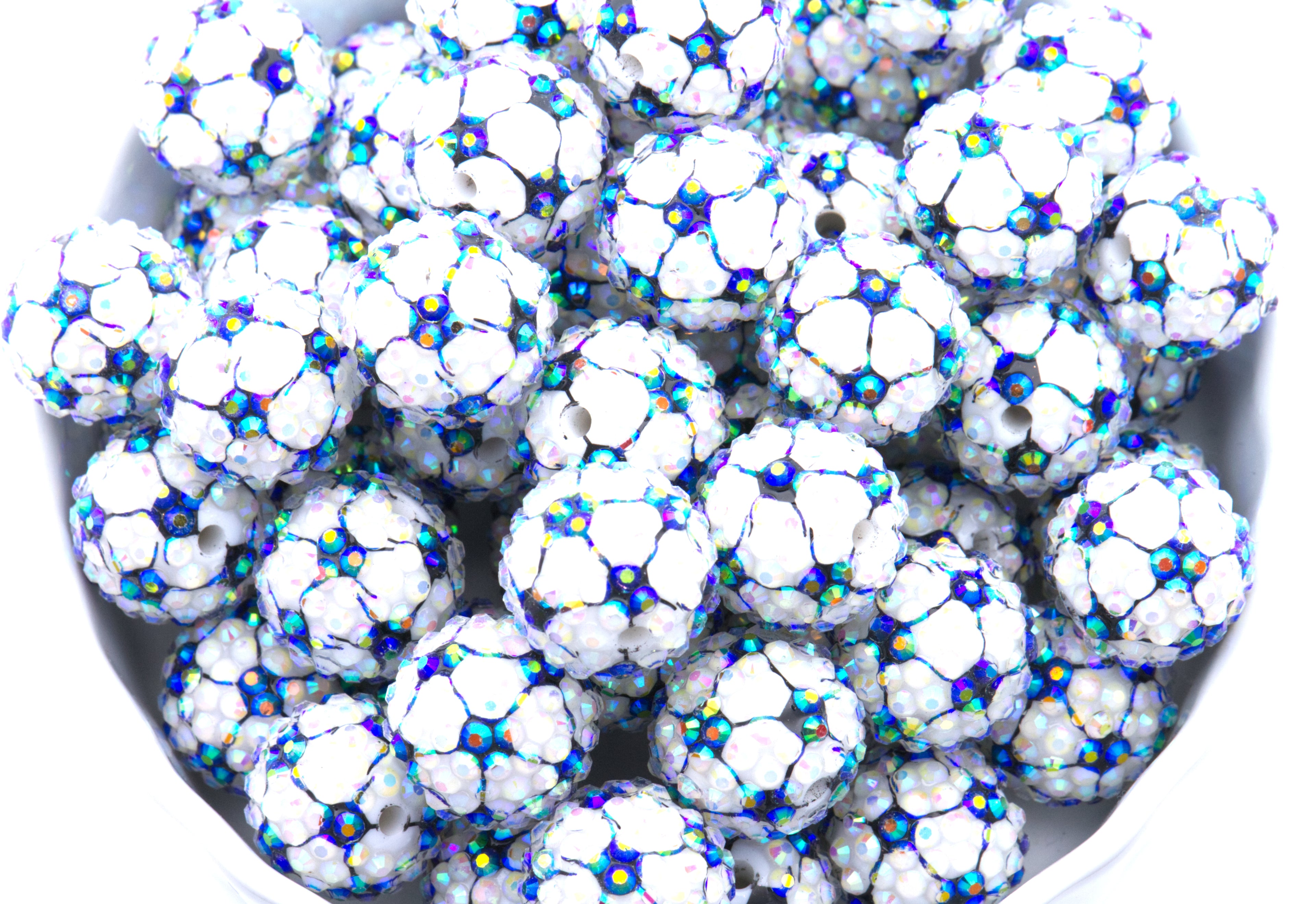 A close-up of soccer ball rhinestone beads, piled inside a white bowl on a white background.
