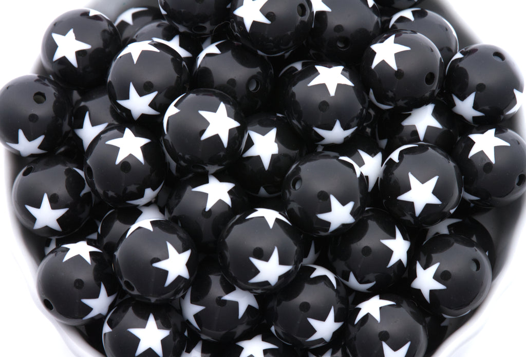 A close-up pile of  black round beads with a white star print set against a clean white background.
