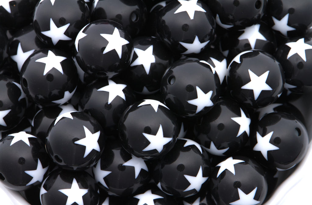 A close-up pile of  black round beads with a white star print set against a clean white background.