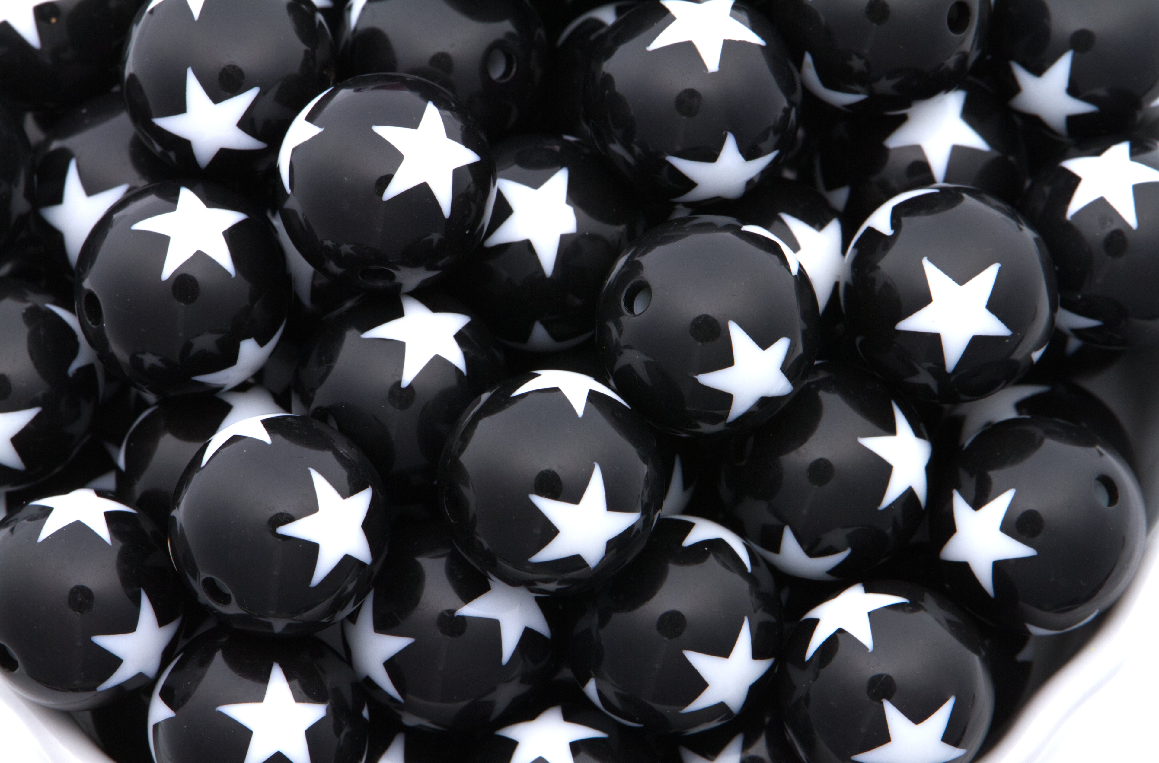 A close-up pile of  black round beads with a white star print set against a clean white background.