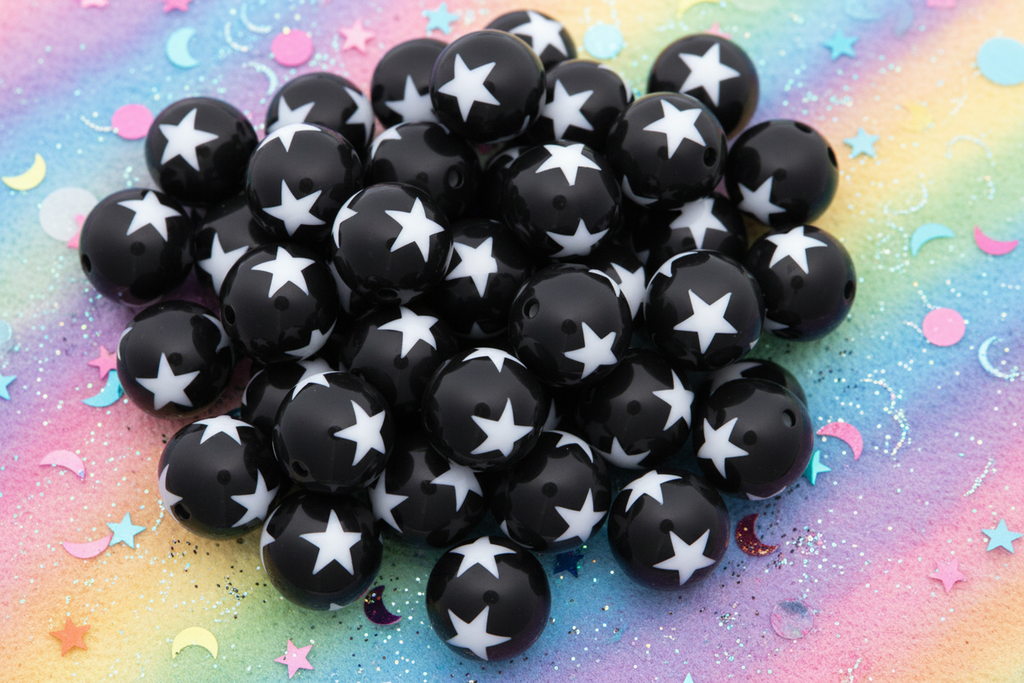 A pile of black round beads with a white star pattern arranged on a colorful pastel background with star and moon confetti.
