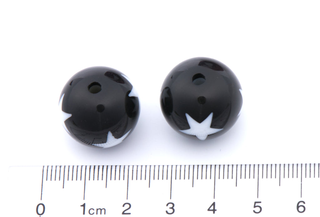 Two small black round beads with white star print, shown next to a cm ruler for scale on a white background.