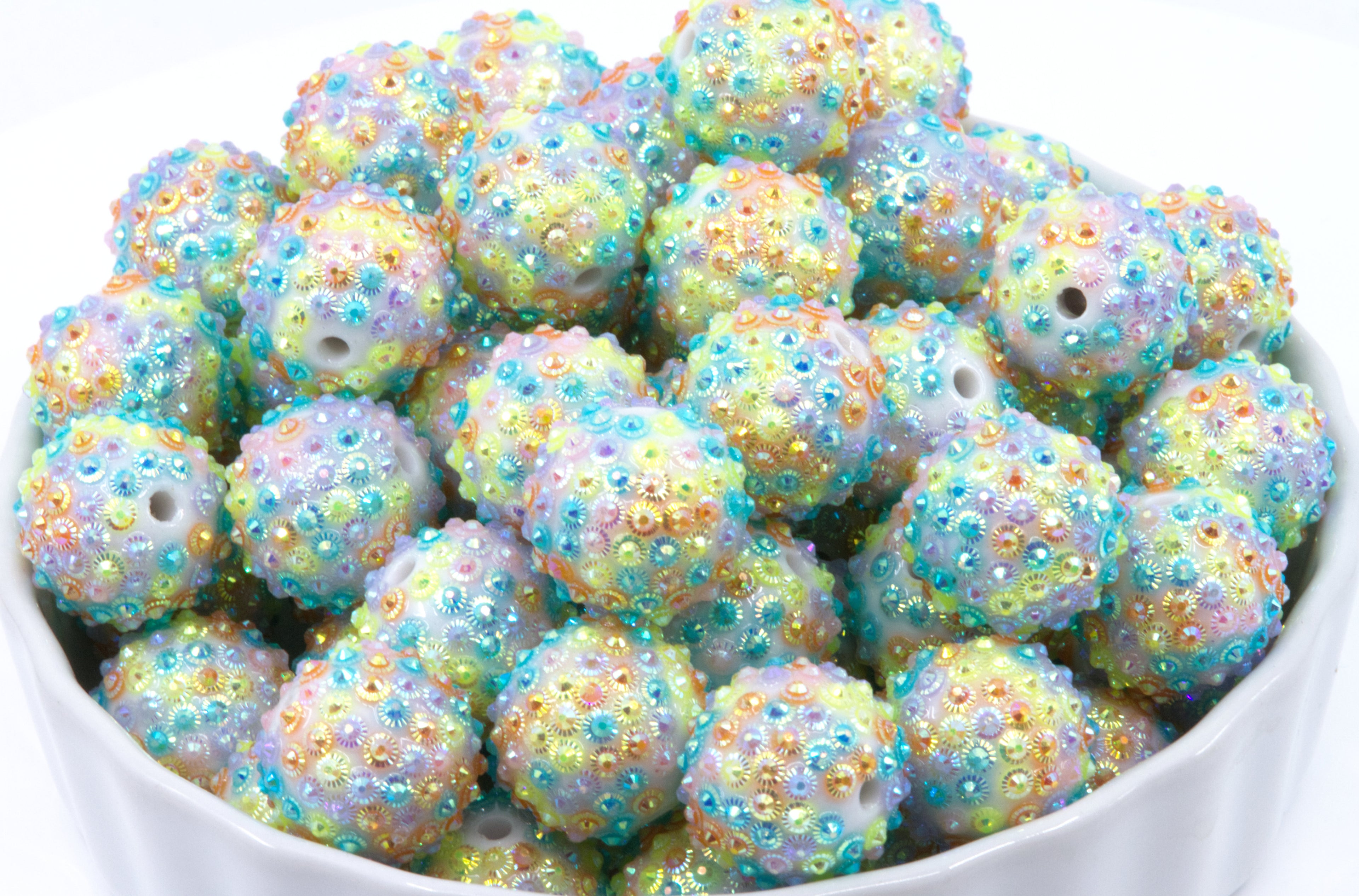 rainbow rhinestone beads in a white bowl on a white background 