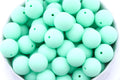 A close-up of many matte mint-green round beads, piled inside a white bowl against a white background.