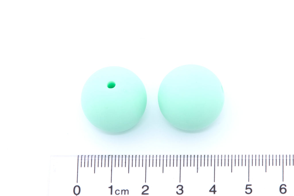 Two mint green beads, displayed above a cm ruler for scale on a white background.