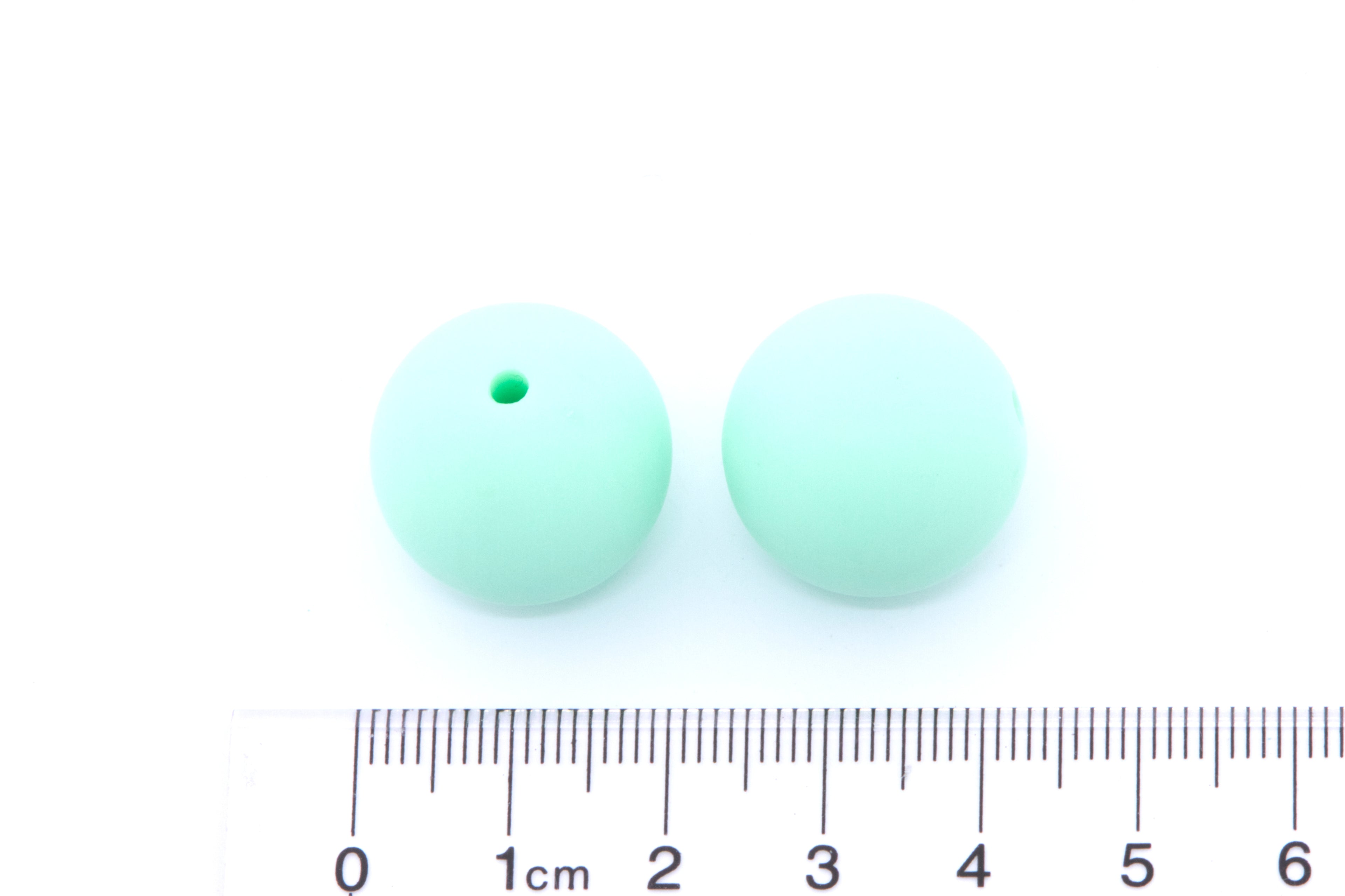 Two mint green beads, displayed above a cm ruler for scale on a white background.