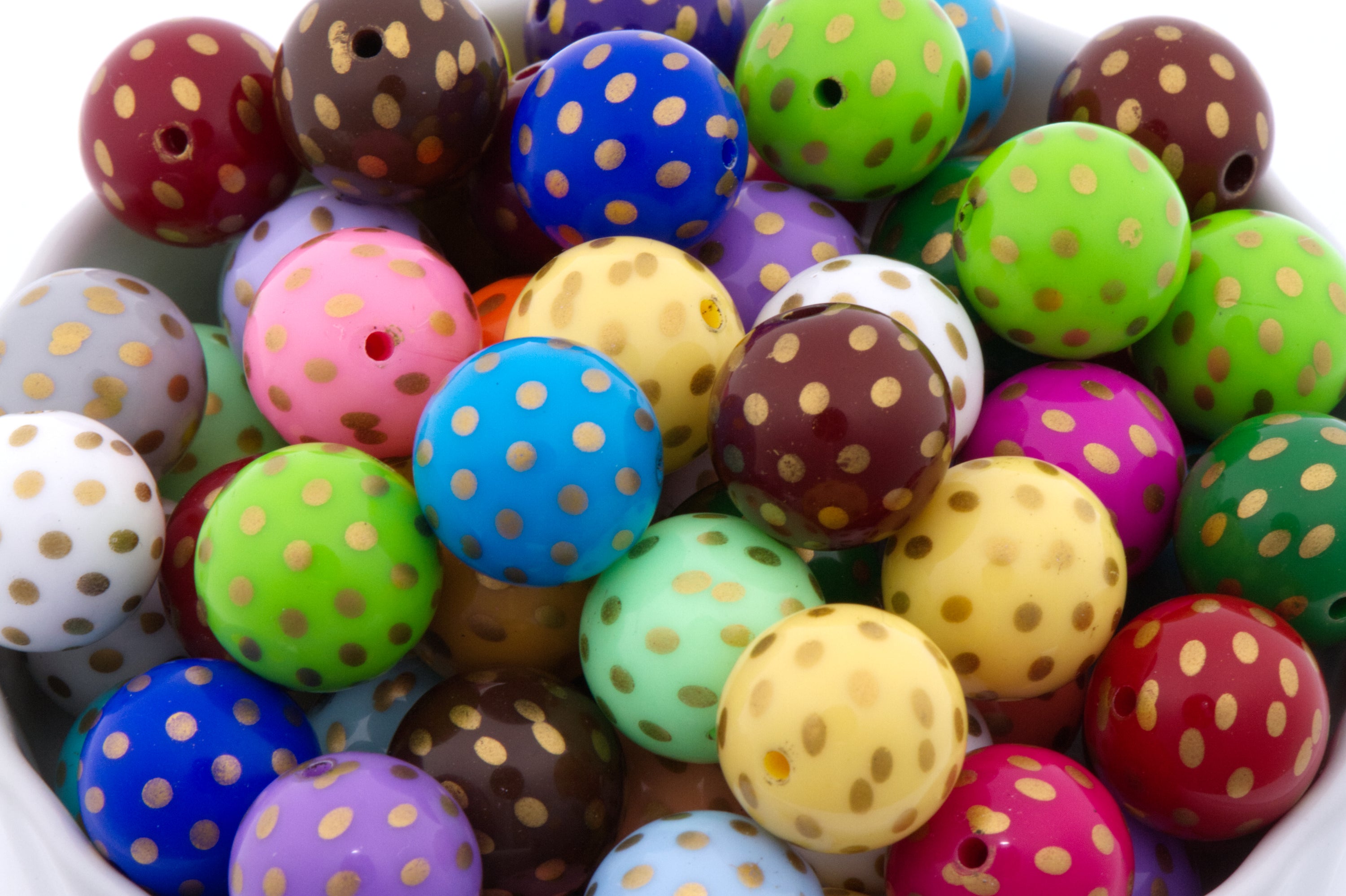 A close-up of colorful round beads with small gold polka dots, arranged in a white container. The beads come in many colors including blue, green, pink, yellow, purple, brown, red, and white.