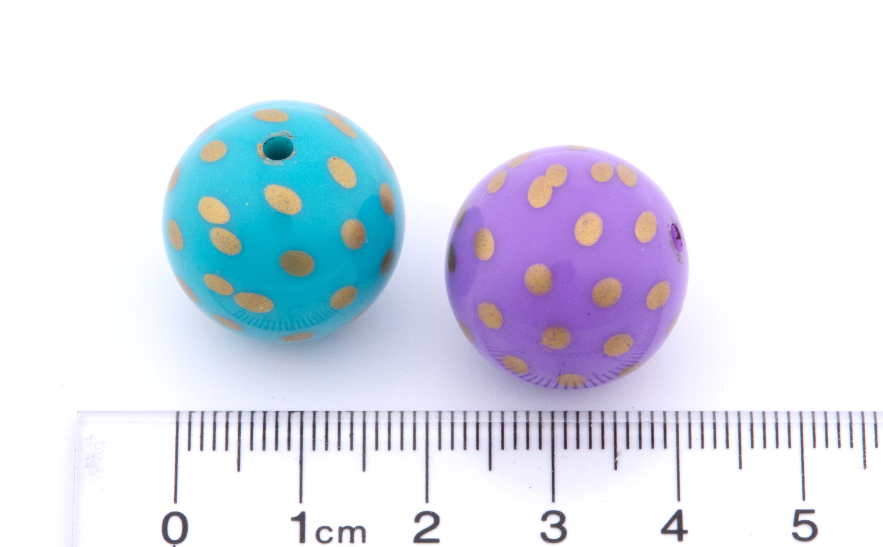 Two round beads with gold polka dots, one turquoise blue and one lavender purple, shown next to a cm ruler for scale on a white background.
