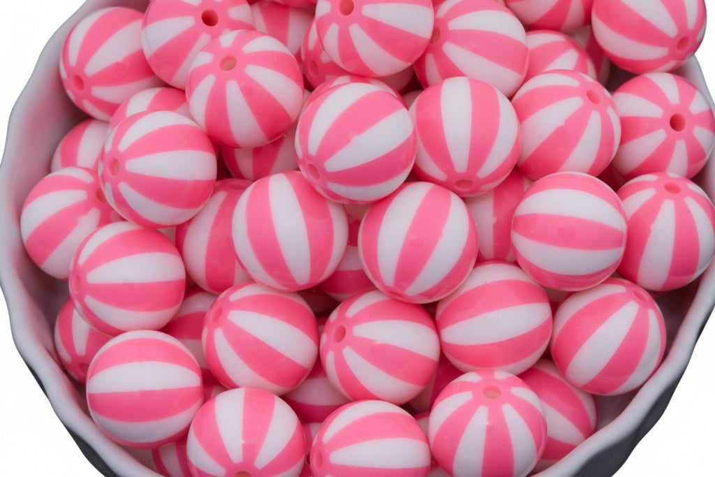 A close-up of many round pink-and-white striped beads  piled in a white bowl against a white background.