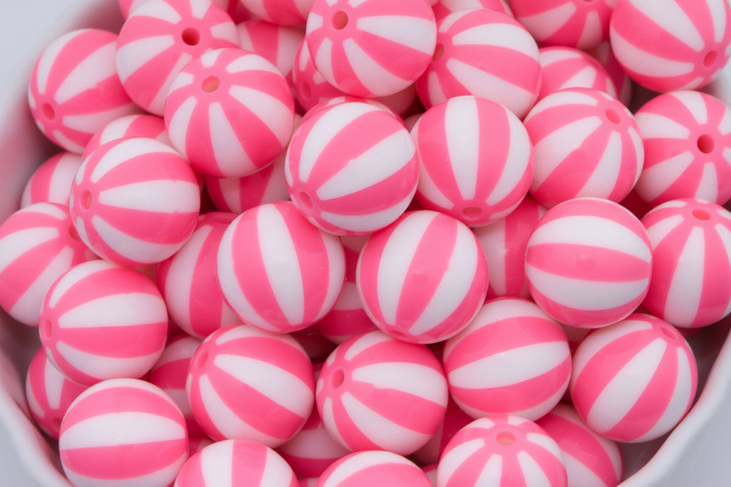 A close-up of many round pink-and-white striped beads  piled in a white bowl against a white background.