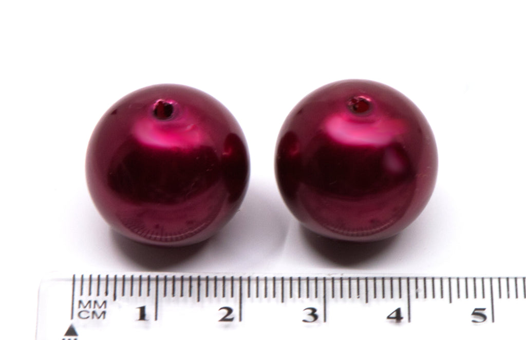 Two shiny metallic deep red round bubblegum beads shown next to a cm ruler for scale on a white background.
