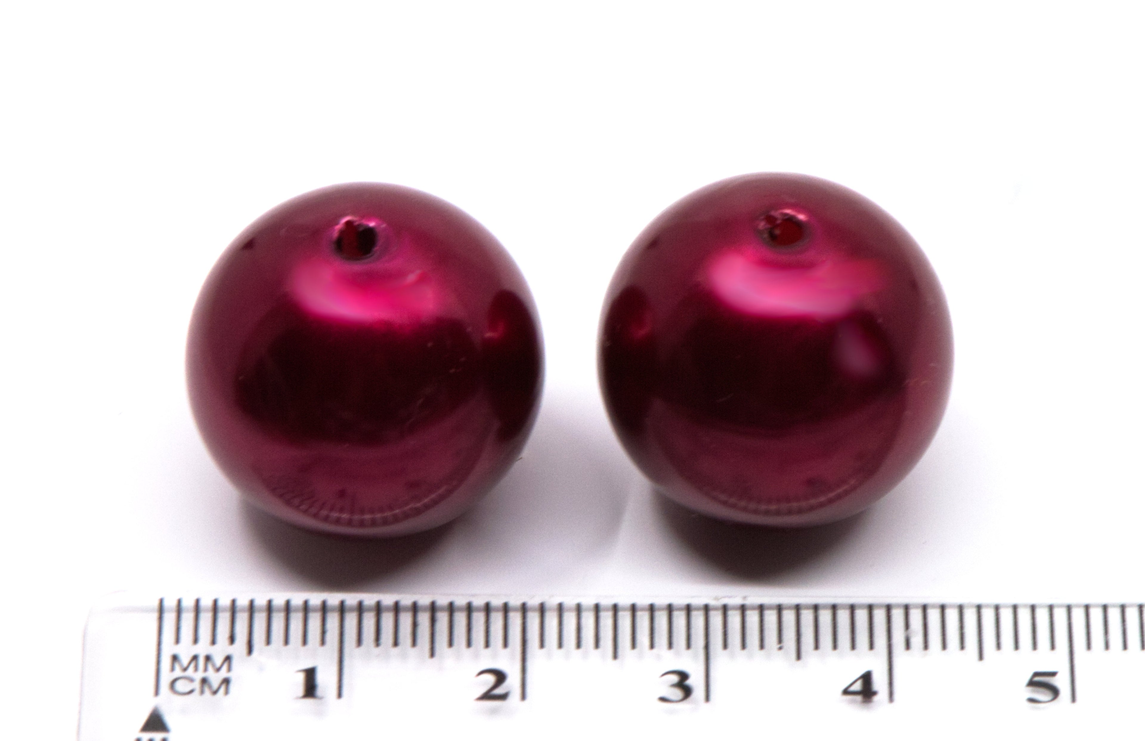 Two shiny metallic deep red round bubblegum beads shown next to a cm ruler for scale on a white background.