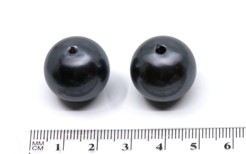 two gray bubblegum beads next to a ruler for scale on a white background 