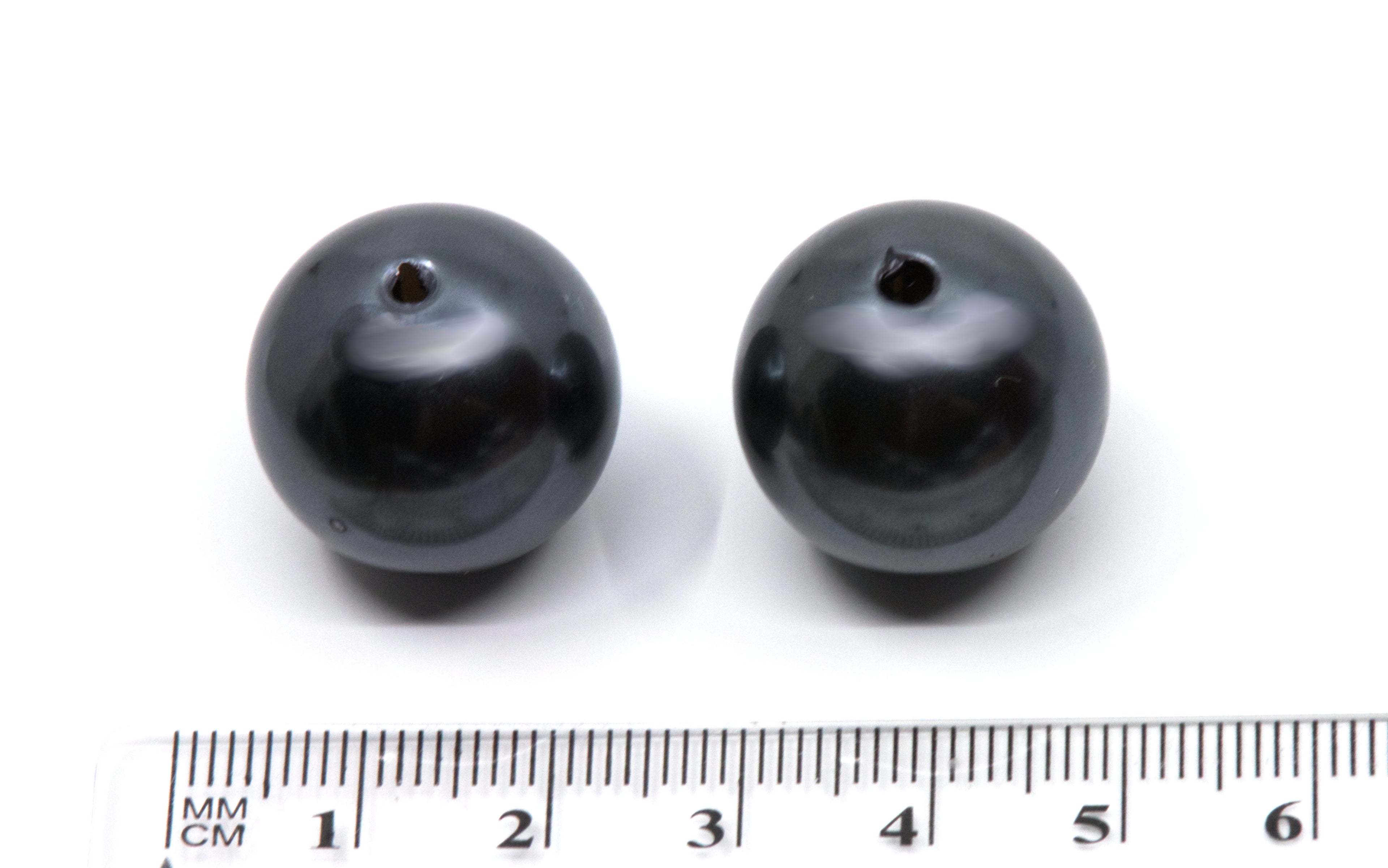 two gray bubblegum beads next to a ruler for scale on a white background 