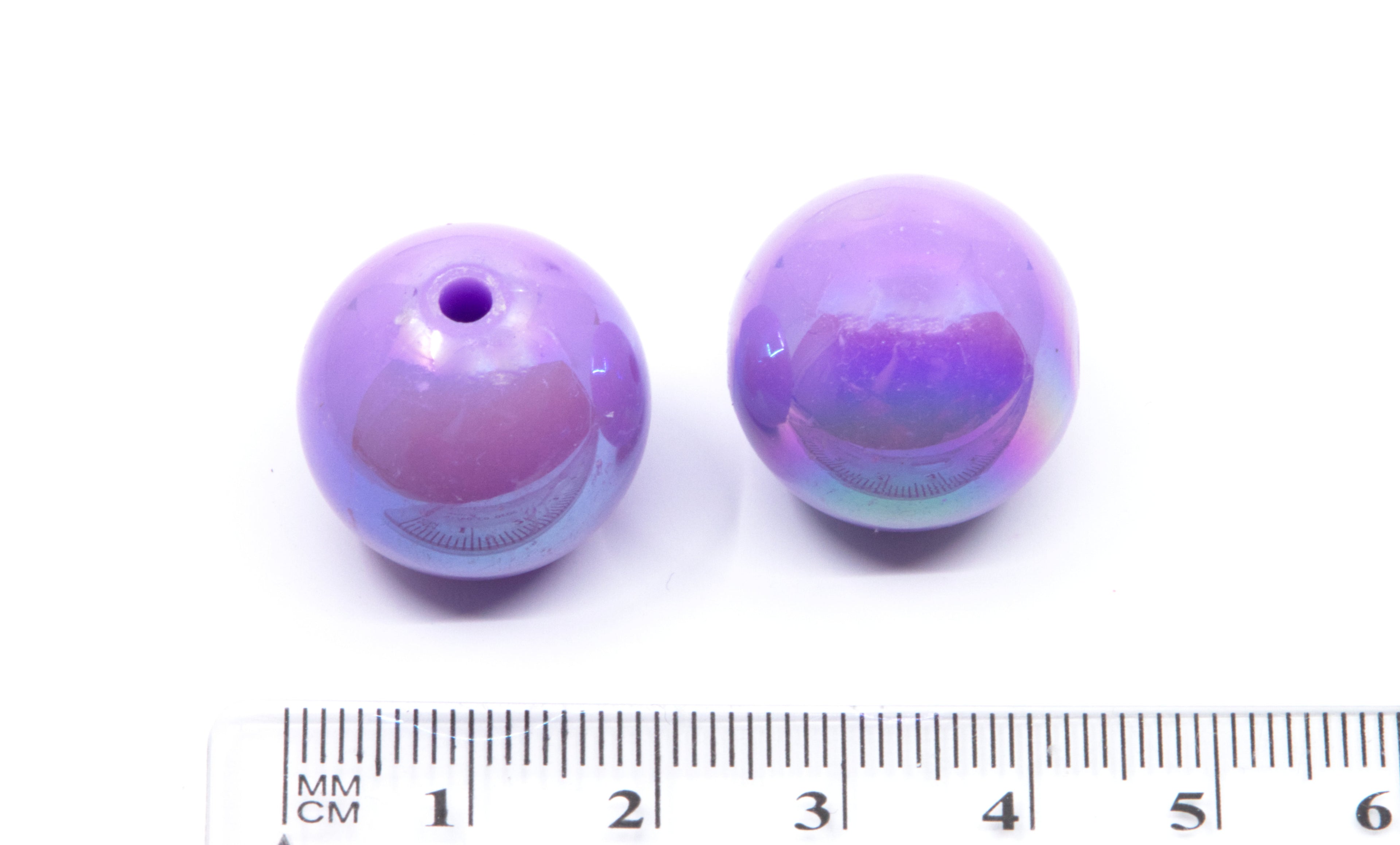 Two purple iridescent beads with a ruler for scale on a white background